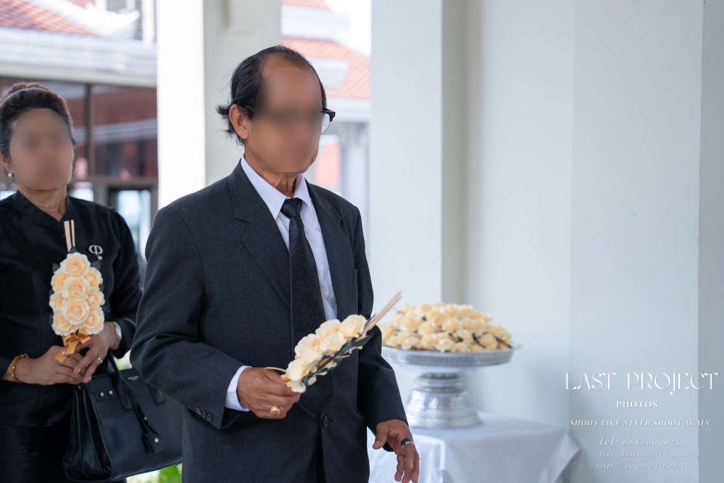เจ้าภาพงานศพถือดอกไม้จันทน์ประดิษฐ์จากกระดาษเดินเข้าสู่พิธีวางดอกไม้จันทน์บนเมรุวัดไทย Funeral hosts holding paper-crafted sandalwood flowers walking towards the crematorium during a Thai Buddhist cremation ceremony