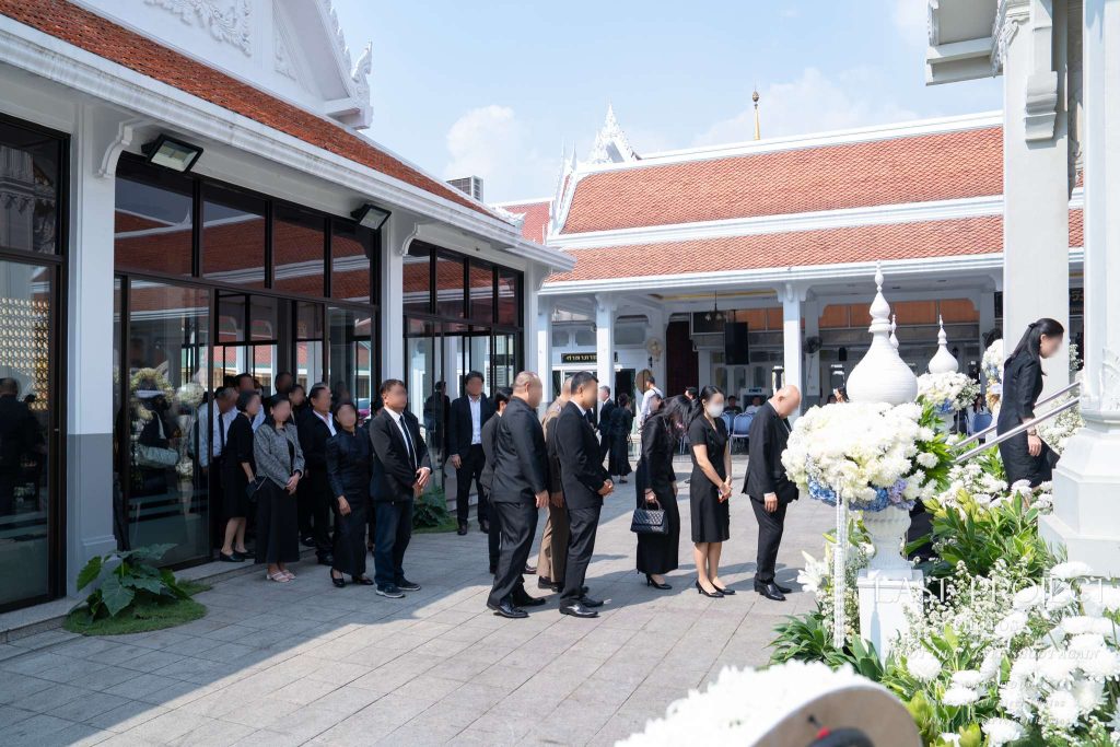 แขกผู้มีเกียรติต่อแถวเพื่อขึ้นวางดอกไม้จันทน์ในพิธีฌาปนกิจศพ ณ เมรุวัดไทย Mourners lining up to place sandalwood flowers and pay final respects at a Buddhist cremation ceremony in a Thai temple