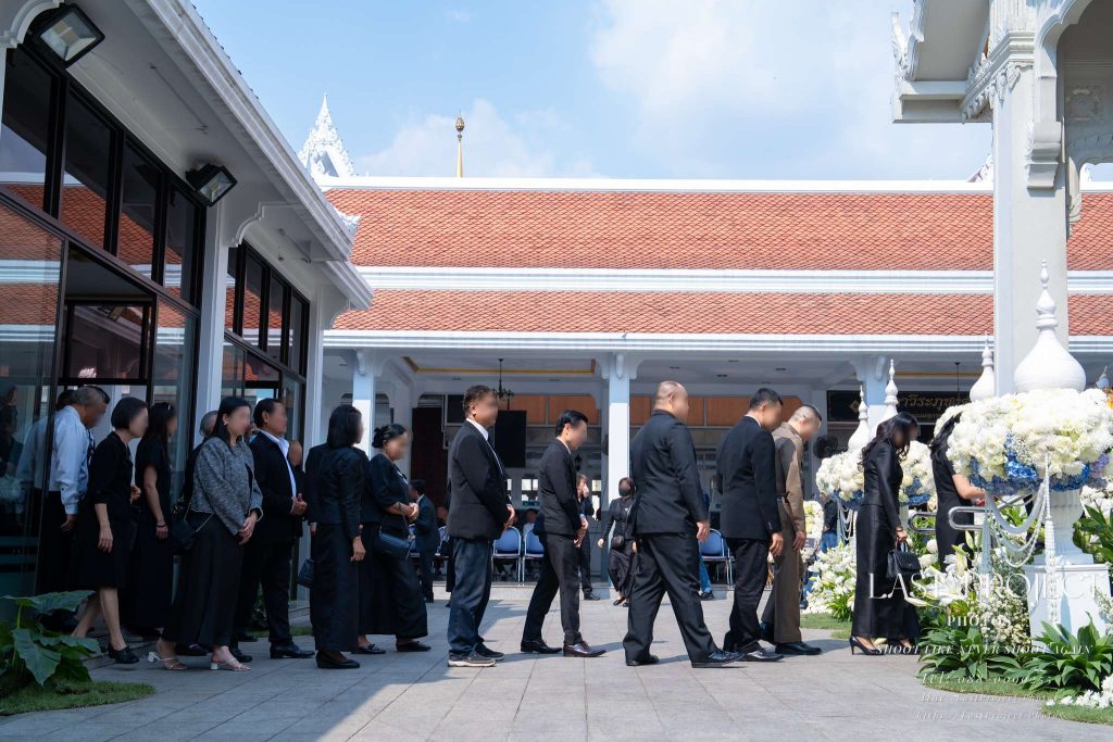 บรรยากาศแขกทยอยต่อแถวขึ้นบันไดเมรุเพื่อวางดอกไม้จันทน์ในพิธีฌาปนกิจศพ Mourners lining up to walk up the crematorium steps for the sandalwood flower placement in a Thai funeral ceremony