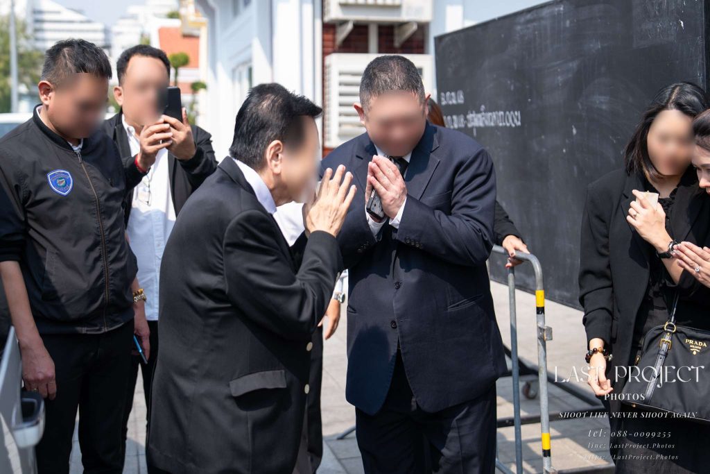 เจ้าภาพยกมือไหว้และเดินส่งแขกผู้ใหญ่ถึงที่รถหลังเสร็จพิธีวางดอกไม้จันทน์ในงานฌาปนกิจศพ The host family respectfully escorting VIP guests to their car and exchanging wais after the Thai cremation ceremony