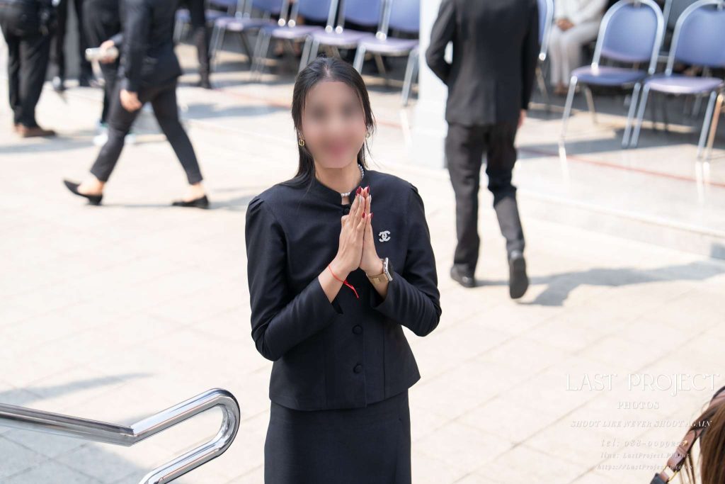 เจ้าภาพสวมชุดไทยไว้ทุกข์สีดำยกมือไหว้ขอบคุณแขกบริเวณทางลงเมรุ Thai funeral host in black mourning attire performing the Wai to thank guests at the crematorium stairs